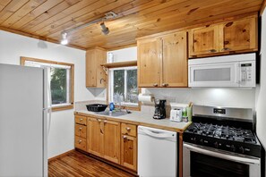 A compact kitchen with wooden cabinets, a microwave, a gas stove, a dishwasher, and a window with blinds. - Secluded Dog Friendly Cabin in Wine Country Cobb California (Cobb)
