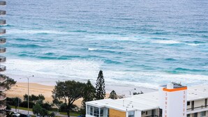 Vista costera con olas del océano, una playa de arena y un edificio con balcones que dan al mar.