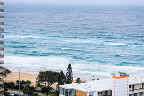 Blick auf die Küste mit Meereswellen, einem Sandstrand und einem Gebäude mit Balkonen, das auf das Meer blickt.