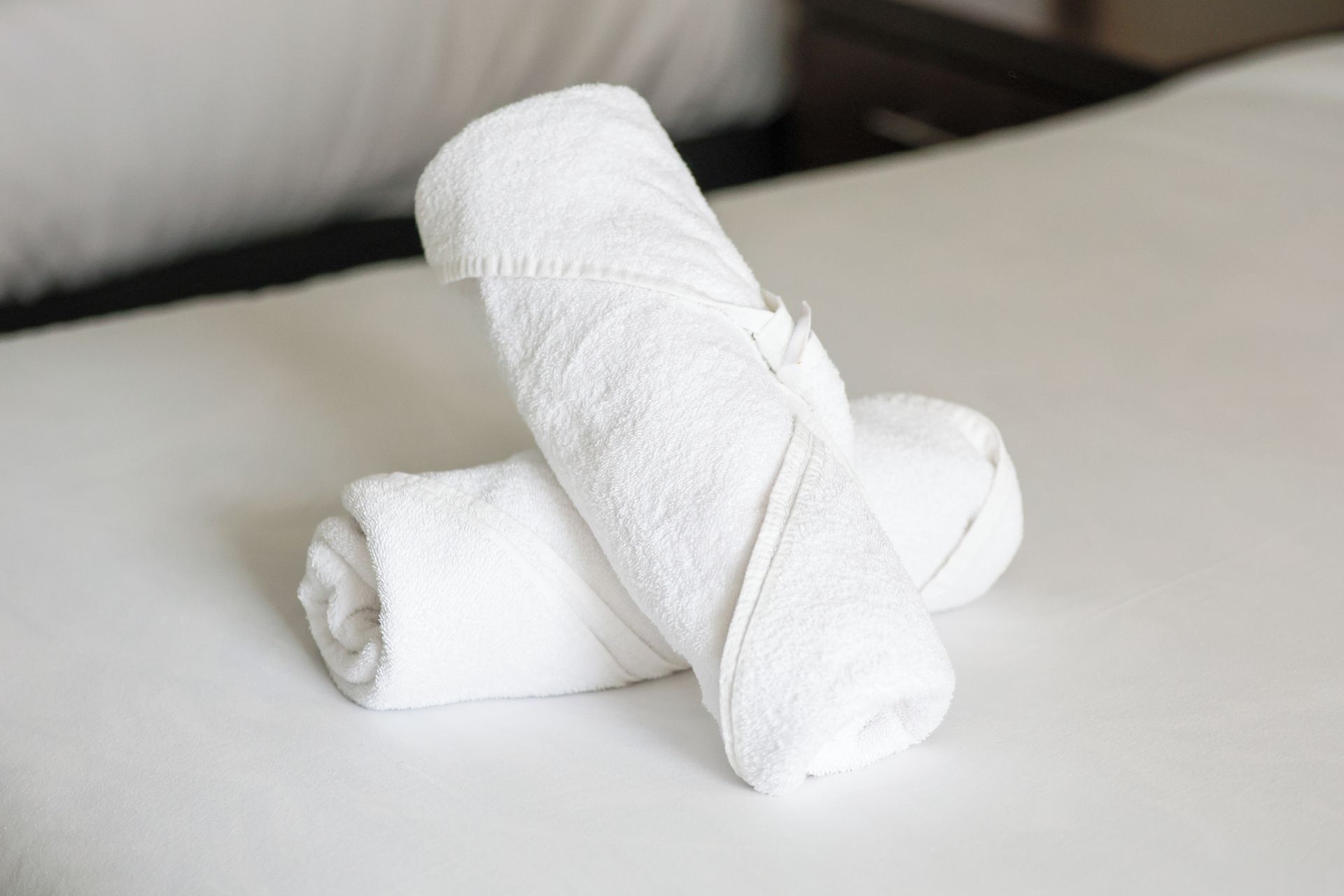 Ein ordentlich gefaltetes weißes Handtuch auf einem Bett mit einem weißen Kissen.