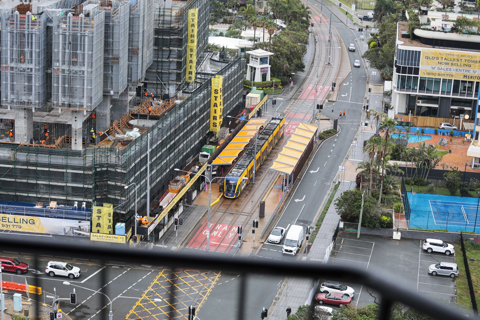 A city street with a tram line, construction site, and buildings including a sales center.
