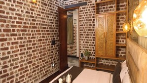 Una habitación con pared de ladrillo, una cama con cabecera de madera, un ventilador de techo y una mesita de noche con una bandeja de objetos.