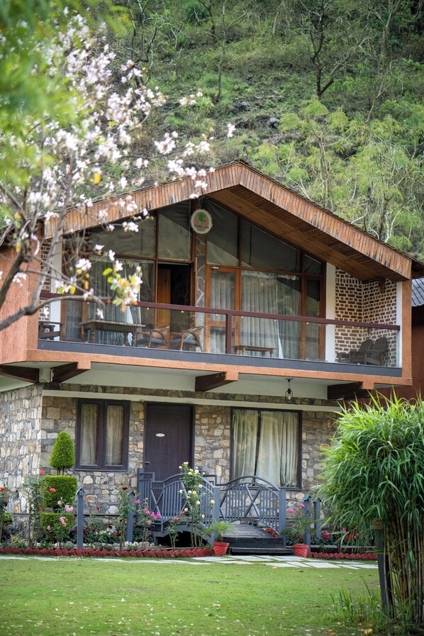 A two-story stone building with a balcony, a stone entrance, and a garden with potted plants.