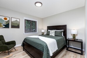 A bedroom with a bed, a chair, a nightstand, a lamp, a window with blinds, and two framed pictures on the wall. - Cozy Cottage with Fire Pit and Barbecue in Pigeon Forge, Tennessee (Pigeon Forge)