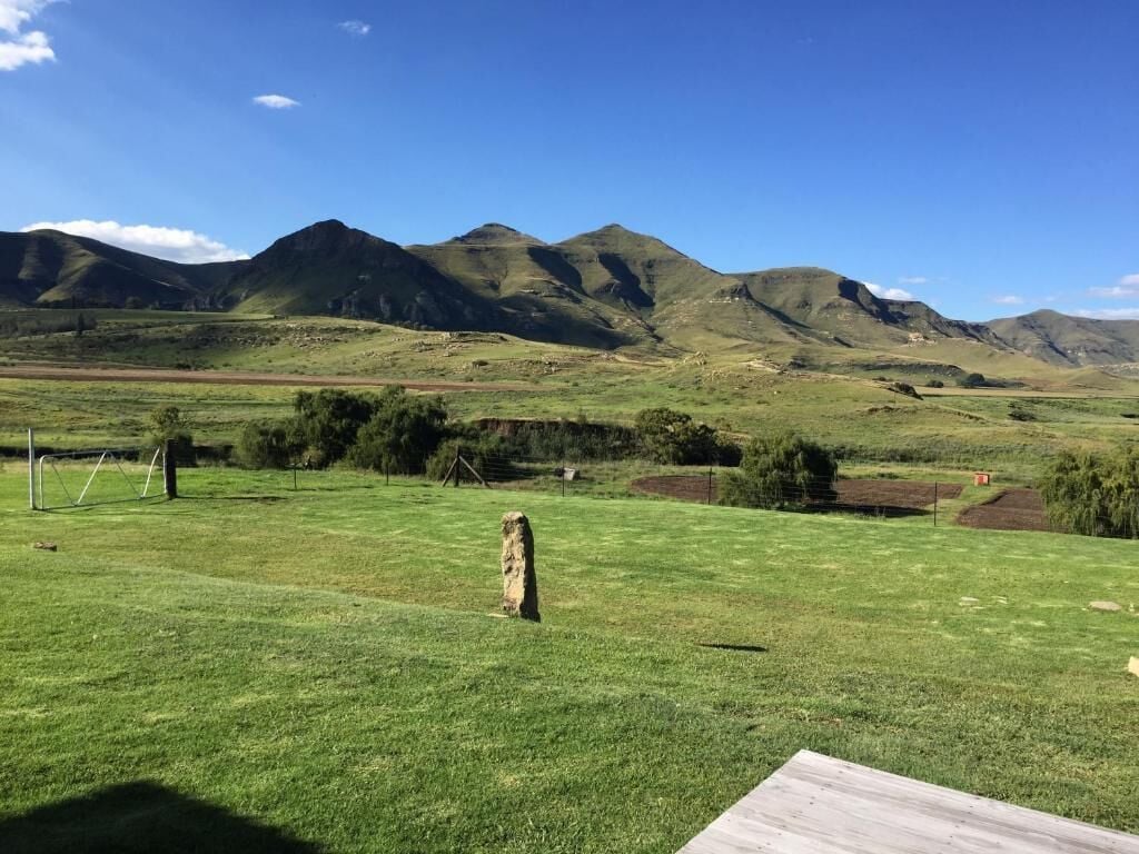 A grassy field with a wooden structure in the foreground and mountains in the background.