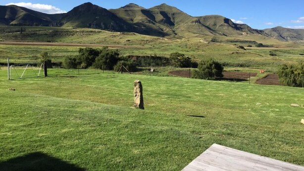 Un campo cubierto de hierba con una estructura de madera en primer plano y montañas al fondo.