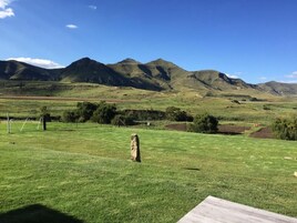 A grassy field with a wooden structure in the foreground and mountains in the background.