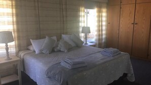 Un dormitorio con cama, mesitas de noche, lámpara, armario y ventana con cortinas.