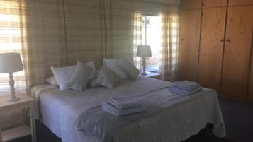 Une chambre à coucher avec un lit, des tables de chevet, une lampe, une armoire et une fenêtre avec des rideaux.