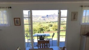 Un comedor con mesa y sillas de madera, una alfombra estampada y vista a un paisaje verde a través de puertas abiertas.