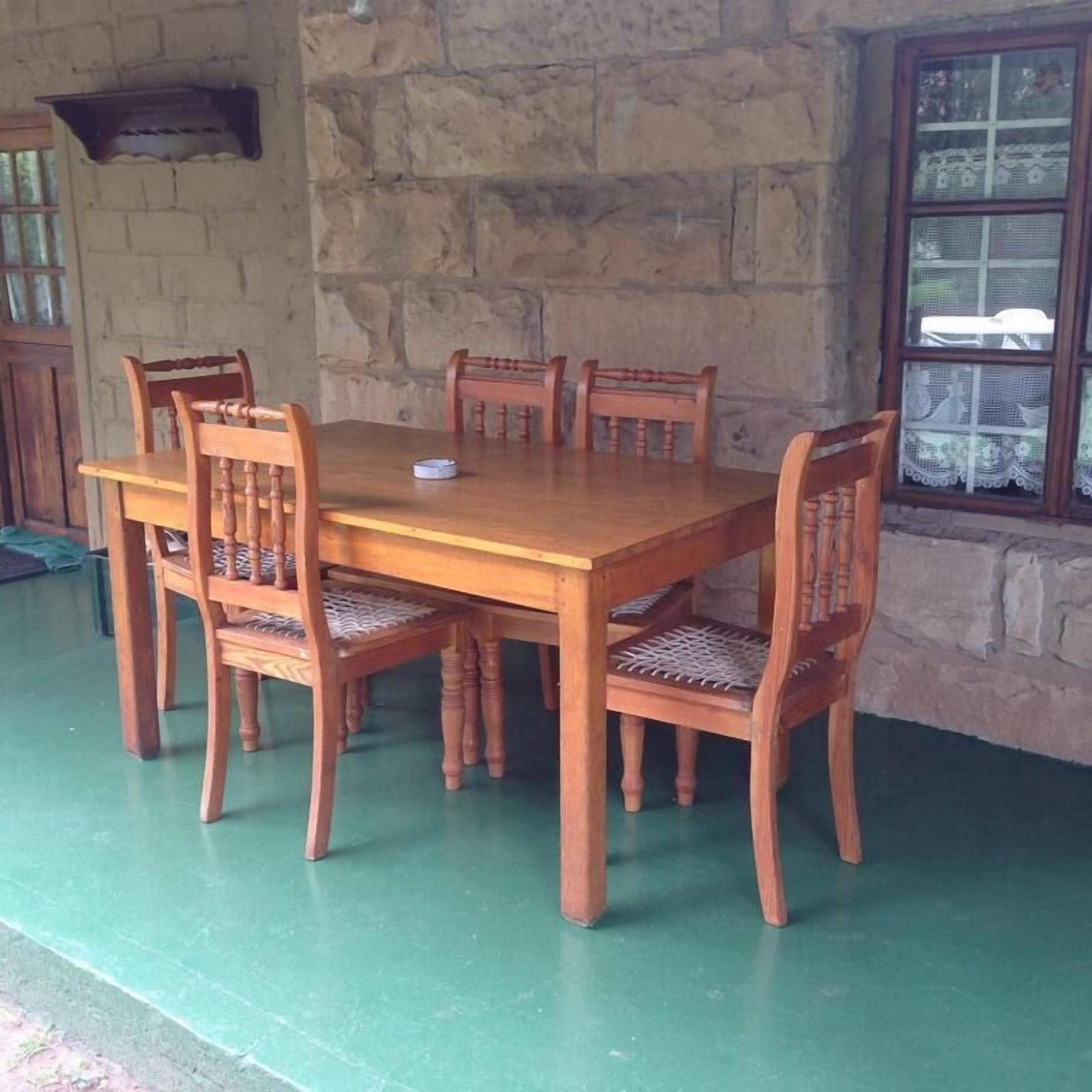 Une table à manger en bois, entourée de six chaises, placée devant un mur de pierre et une fenêtre ornée de rideaux en dentelle.