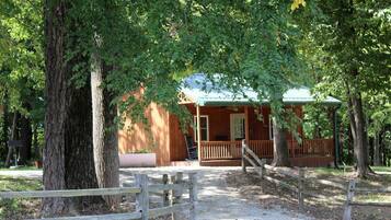 A rustic wooden cabin with a porch, surrounded by trees.