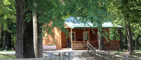 A rustic wooden cabin with a porch, surrounded by trees.