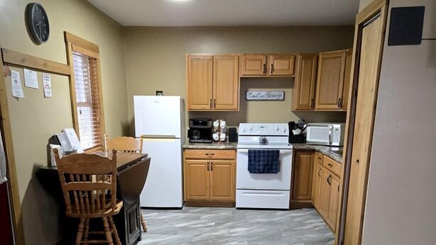 A compact kitchen with wooden cabinets, a refrigerator, a stove, and a dining area with a chair.