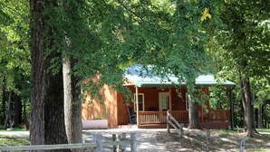 A rustic wooden cabin with a porch, surrounded by trees.