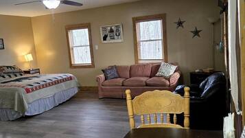 A bedroom with a bed, a wooden dining table, a ceiling fan, and a window.