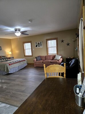 A bedroom with a bed, a wooden dining table, a ceiling fan, and a window.