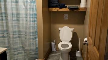 A bathroom with a toilet, shower curtain, and a shelf with towels.