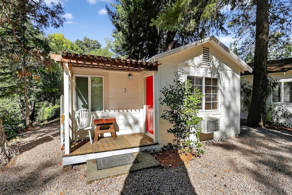 A small, single-story house with a porch, a red door, and a number '3' on the wall.