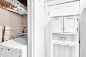 Une buanderie équipée d’un lave-linge, d’un sèche-linge et de meubles blancs.