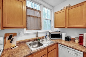 A kitchen with wooden cabinets, a granite countertop, a sink, a microwave, a toaster, and a dishwasher. - C.A.L.M. Cottage at the Last Mile Savannah, GA Vacation Rental (Savannah)