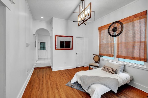 A bedroom with a bed, a chair, a window with blinds, a mirror, and a door. - C.A.L.M. Cottage at the Last Mile Savannah, GA Vacation Rental (Savannah)