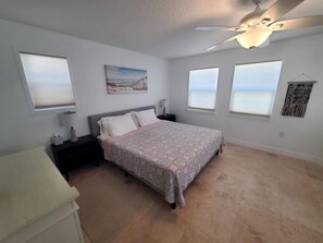 A bedroom with a bed, a nightstand, a ceiling fan, and a window with a view.