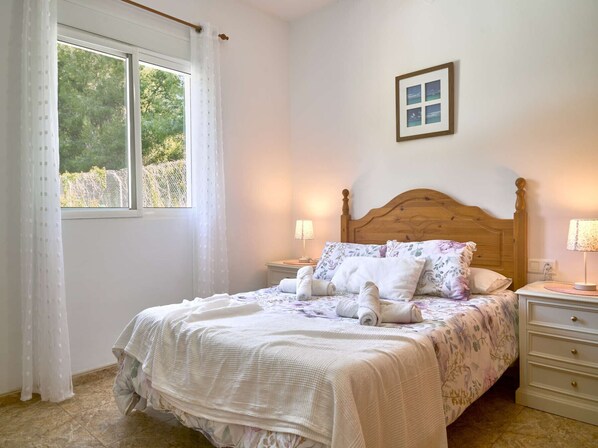 A bedroom with a bed, two bedside tables, a window with curtains, and a framed picture on the wall. - Conjunto Rural Las Rosas 1 by Casasol (Frigiliana)