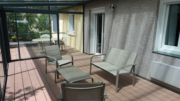 Eine überdachte Terrasse mit Gartenmöbeln, einer Ziegelwand und einer Schiebetür.