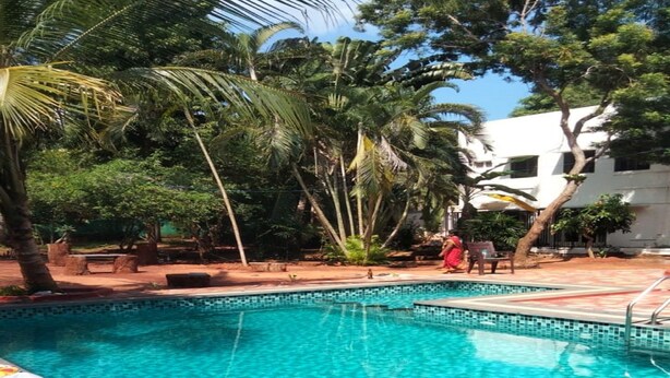 Ein Swimmingpool mit klarem, blauem Wasser, umgeben von Palmen und einem Gebäude im Hintergrund.