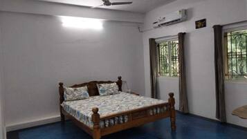 Une chambre à coucher avec un lit en bois, un ventilateur de plafond, un appareil de climatisation et une fenêtre avec des rideaux.