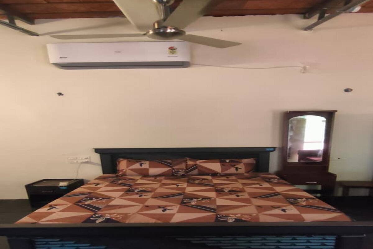 Een slaapkamer met een bed, nachtkastje, kaptafel, spiegel en een airconditioning.
