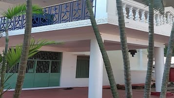 Un edificio con balcón, palmeras y suelo rojo.