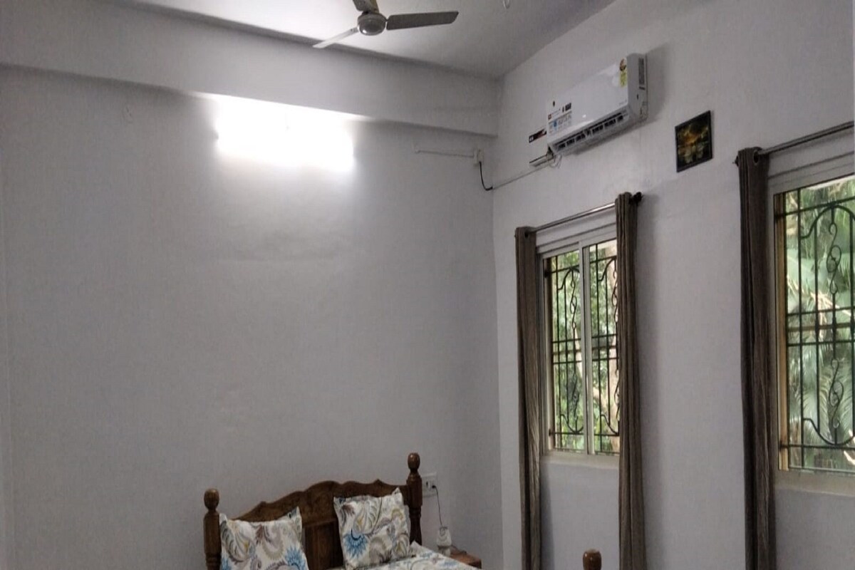 A bedroom with a wooden bed, a ceiling fan, an air conditioning unit, and a window with metal bars.