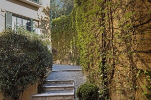 Un stretto vicolo con gradini che conducono a un edificio, circondato da vegetazione lussureggiante e muri ricoperti d'edera.