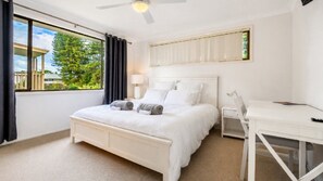 Une chambre à coucher avec un lit, une table de chevet, une lampe et une vue sur la verdure.