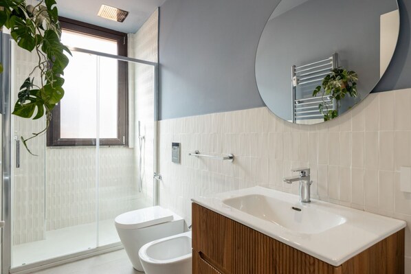 Een moderne badkamer met een glazen douchecabine, een witte wastafel en een houten opbergmeubel.