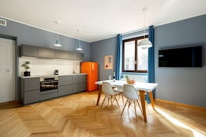 Eine moderne Küche mit grauen Schränken, einem orangefarbenen Kühlschrank und einem Essbereich mit weißem Tisch und Stühlen.