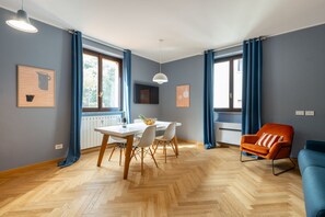 A modern living room with a dining area, large windows with blue curtains, a herringbone wooden floor, and a bright pendant light. - BDC - Tres chic in the heart of Milan! (Milan)