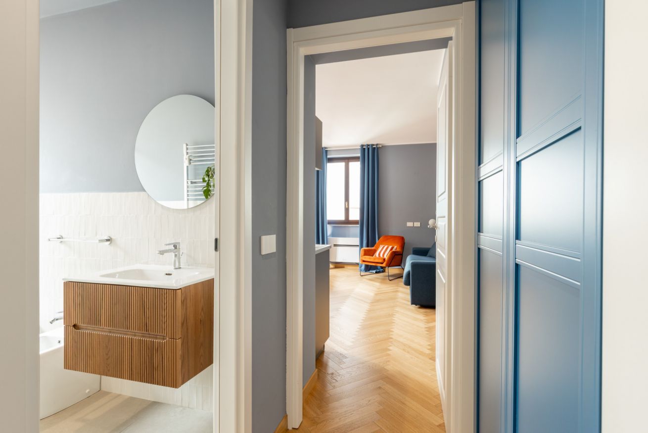 Un baño moderno con tocador de madera, espejo redondo y lavamanos blanco.