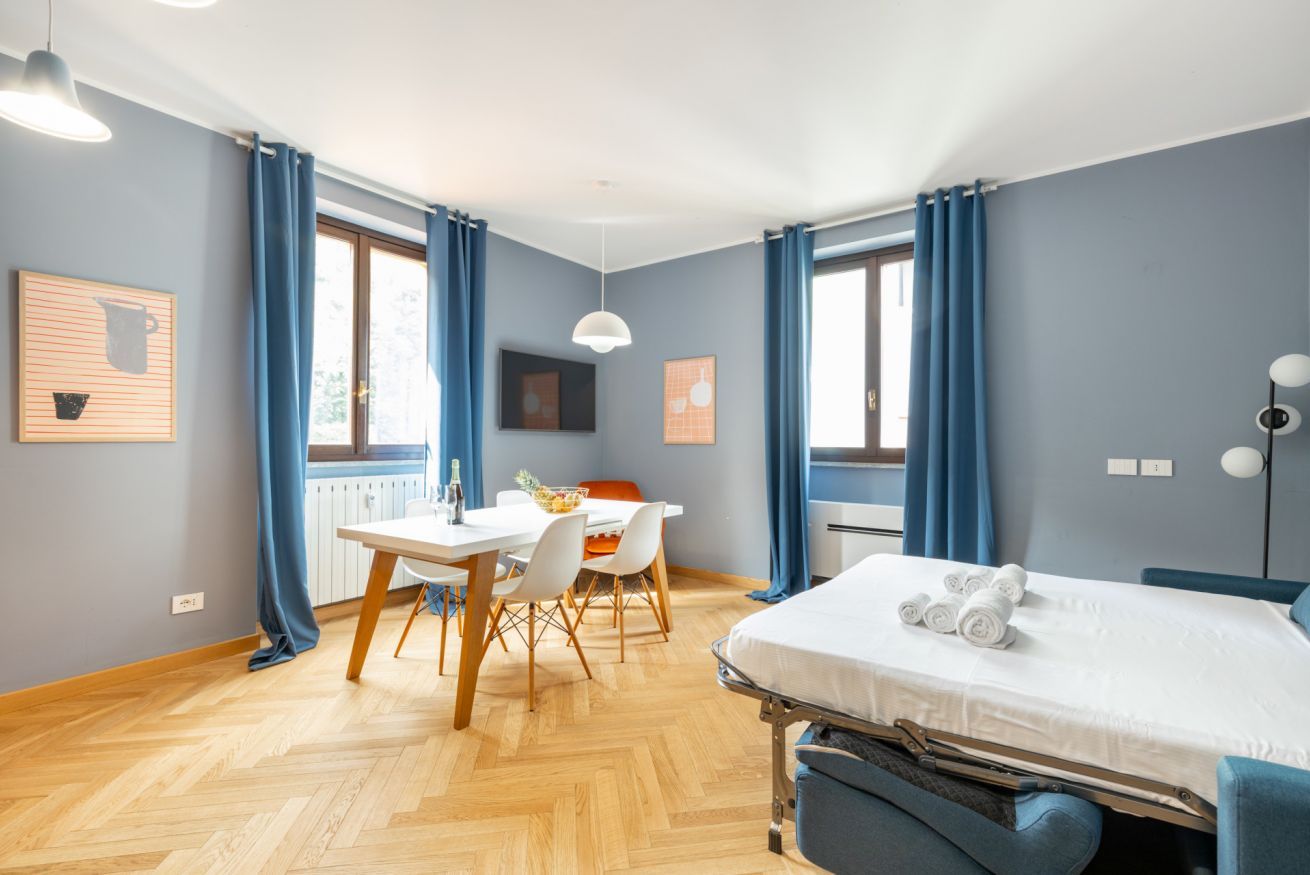 Une chambre d’hôtel moderne équipée d’un lit, d’une table à manger, de chaises, d’un téléviseur et de grandes fenêtres avec des rideaux.