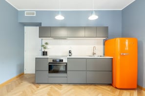 Eine moderne Küche mit grauen Schränken, einer weißen Arbeitsplatte, einem Einbauofen, einer Spüle und einem orangefarbenen Kühlschrank.