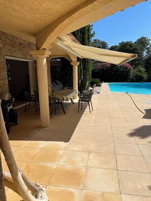 Ein überdachter Patio-Bereich mit Pool, Gartenmöbeln und einer Steinmauer.