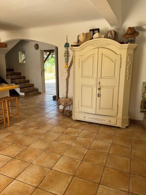 Ein geräumiges Zimmer mit Fliesenboden, einer Holztreppe, einem weißen Schrank mit Verzierungen und einer Tür, die nach draußen führt.