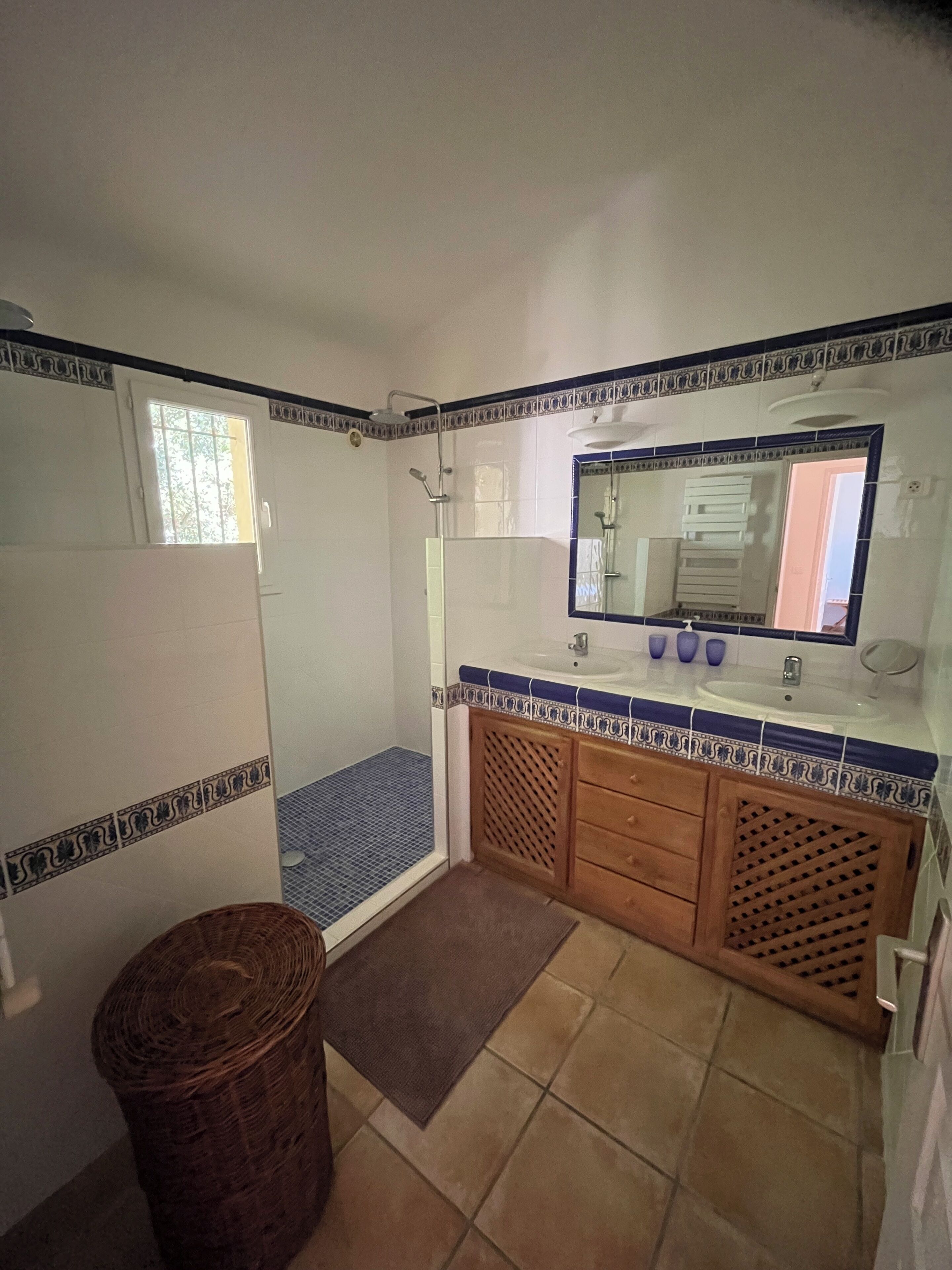 A bathroom with a shower, a sink with a mirror, and a small trash bin.