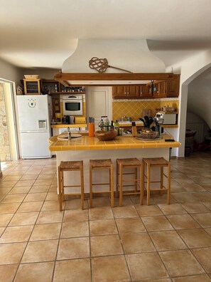 Eine Küche mit einer zentralen Kochinsel, Holzstühlen, einem Kühlschrank, einem Backofen und einer Mikrowelle.
