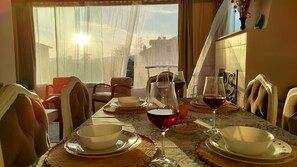 A dining table set with bowls, plates, and wine glasses, with a view of buildings through sheer curtains. - Beautiful Comfy House in Fethiye (Fethiye)