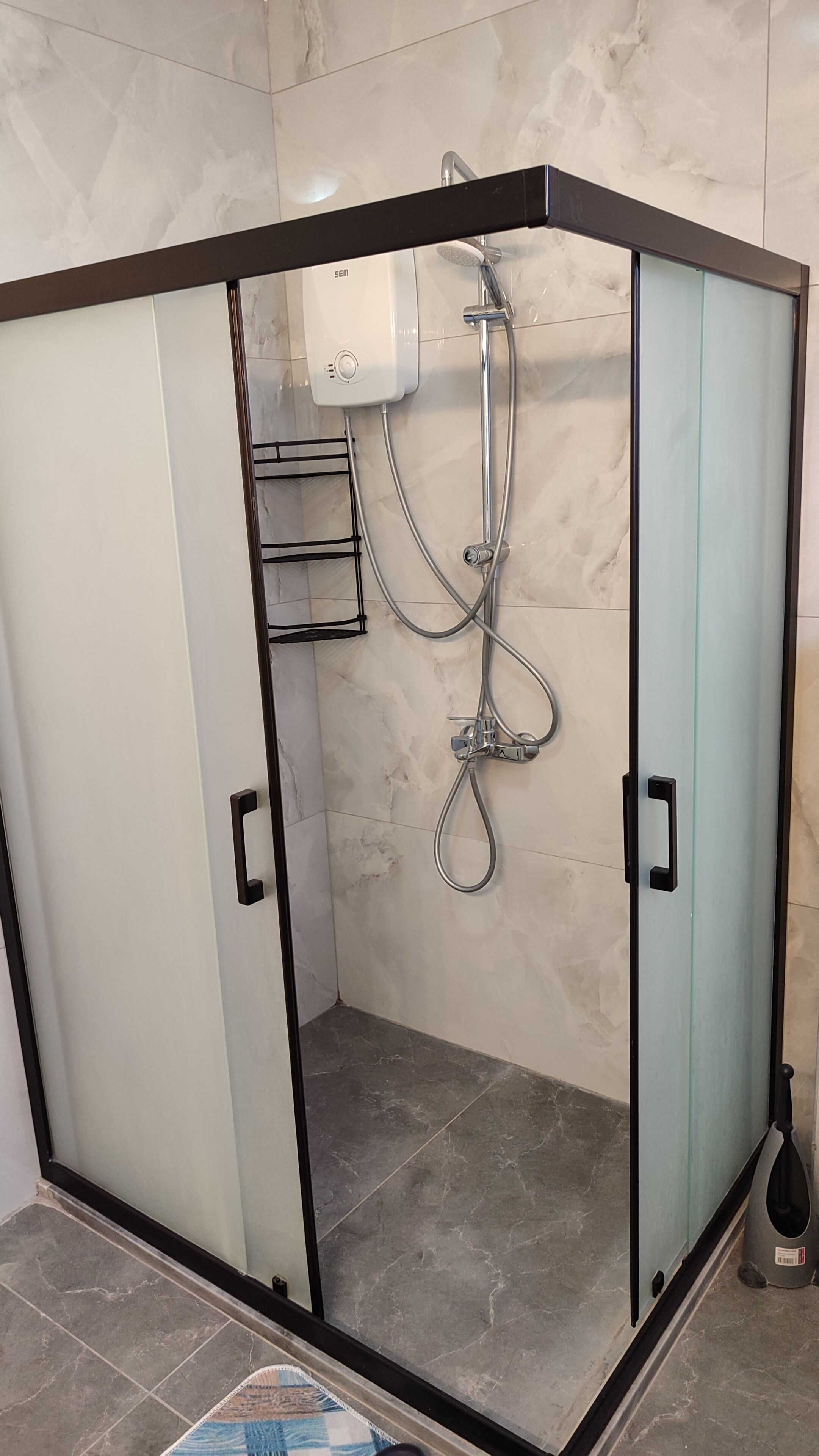 A walk-in shower with a glass door, a handheld showerhead, and a wall-mounted control panel.