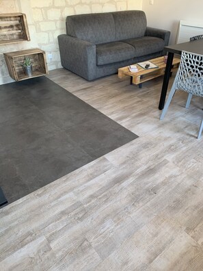 A living room with a grey sofa, a coffee table, a patterned chair, and a grey rug. - 1st-floor apartment (Avoine)