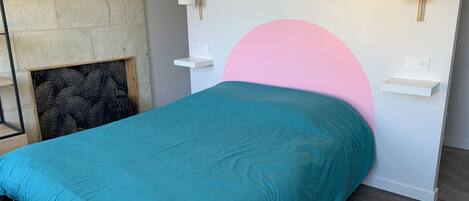 Een bed met een blauwgroene spreidek, een roze hoofdbord en twee nachtkastjes met wandlampen.